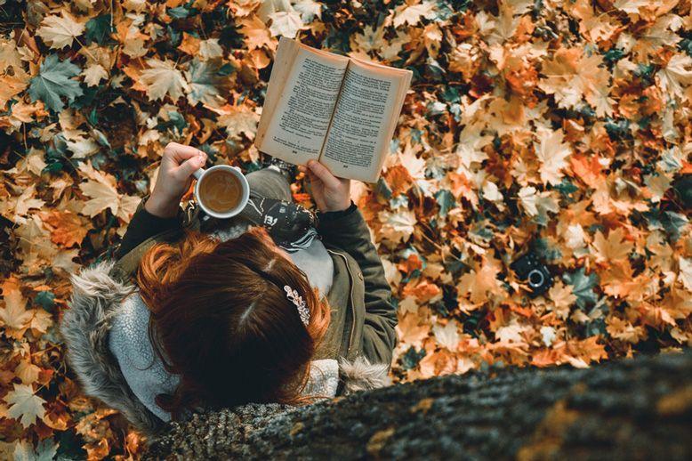 Femme qui lit un livre au pied d'un arbre en automne